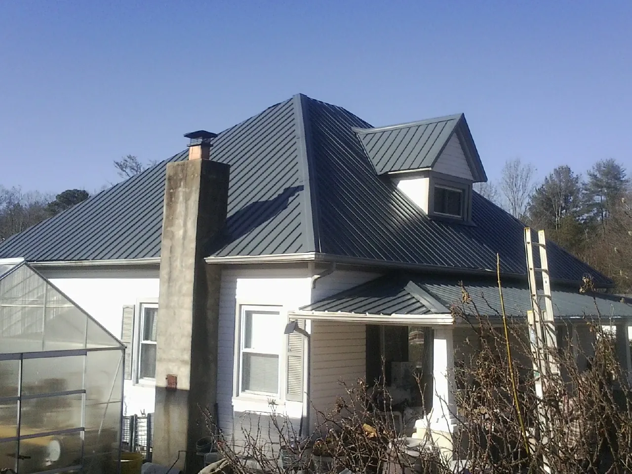 Dark blue standing seam metal roof on a white farmhouse with dormer — Slate & Tile Roof Repair by Roofing Brothers in Petroleum