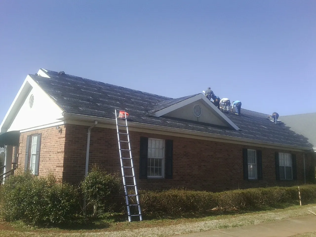 Crew tearing shingles off a brick ranch roof with a ladder set — Metal Roof Repair work by our crew in Petroleum