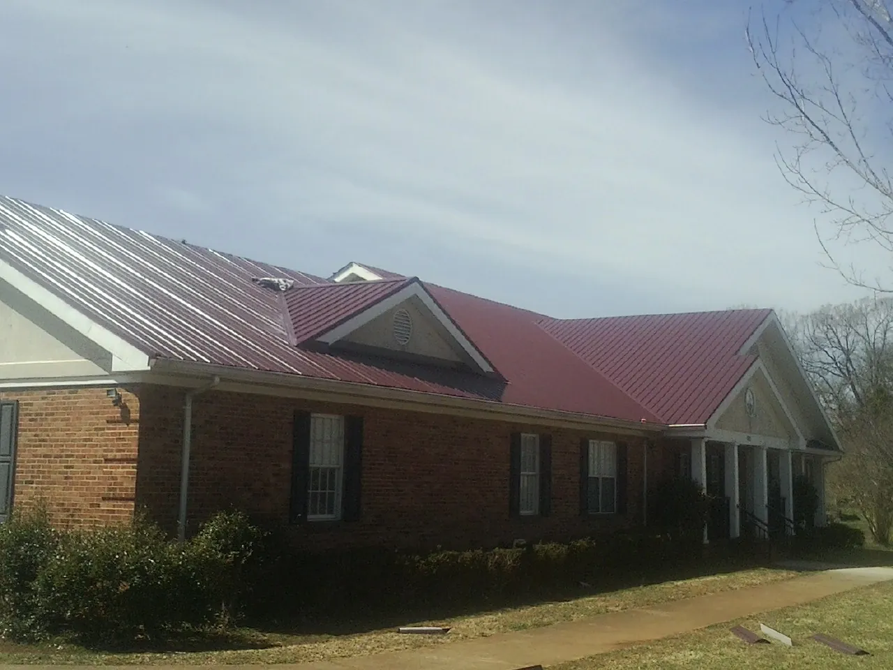 Red metal roof with gabled entries on a long brick building, from a Hail Damage Roof Repair job in Petroleum
