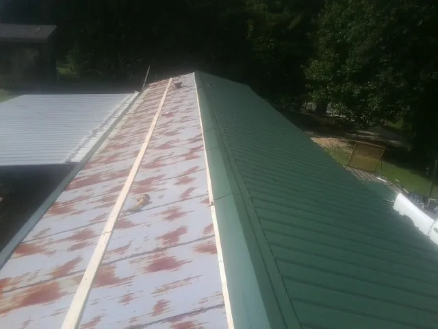 Old rusted panels beside newly installed green metal roofing — Wind Damage Roof Repair by Roofing Brothers in Petroleum