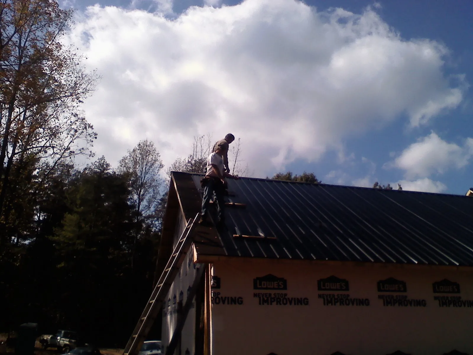 Roofer fastening dark metal panels high against a cloudy sky, from a Roof Inspection job in Petroleum