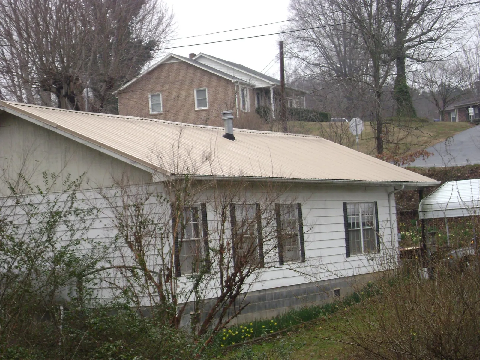 Tan metal roof on a white sided house set into a hillside — Commercial Roofing by Roofing Brothers in Petroleum